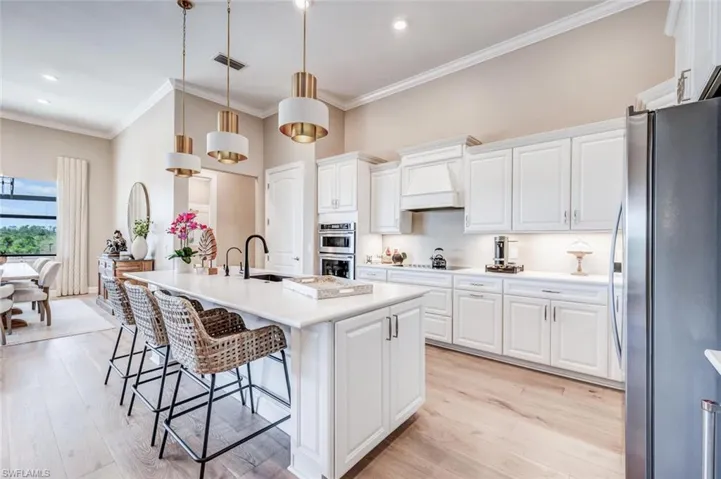 Kitchen featuring light wood-type flooring, pendant lighting, a kitchen island with sink, white cabinetry, and appliances with stainless steel finishes