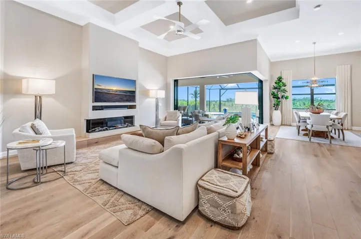 Living room with coffered ceiling, ceiling fan with notable chandelier, and light hardwood / wood-style flooring