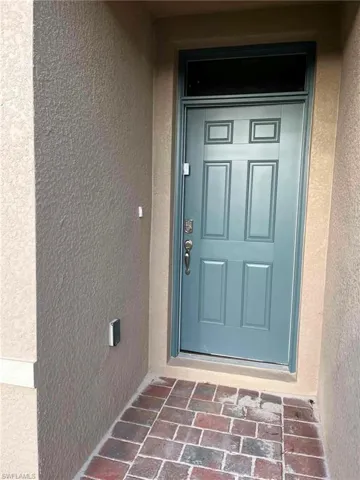Entrance featuring a blue paneled door with transom window, textured stucco exterior, and a brick paver landing