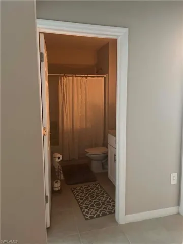 Bathroom featuring a white vanity with a countertop, a toilet, a shower/tub combination with a shower curtain, and tile flooring