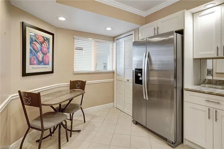 Kitchen with stainless steel refrigerator with ice dispenser, light stone counters, crown molding, light tile patterned floors, and white cabinetry