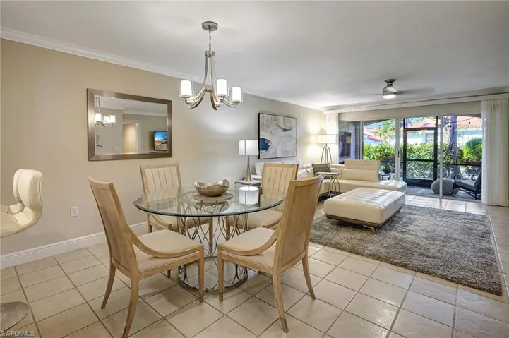Dining space featuring light tile patterned floors, ceiling fan with notable chandelier, and ornamental molding