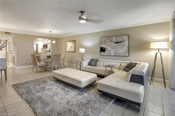 Tiled living room with crown molding and ceiling fan with notable chandelier