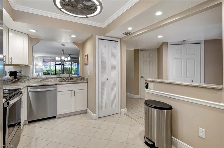 Kitchen featuring white cabinets, ornamental molding, appliances with stainless steel finishes, a notable chandelier, and light stone counters