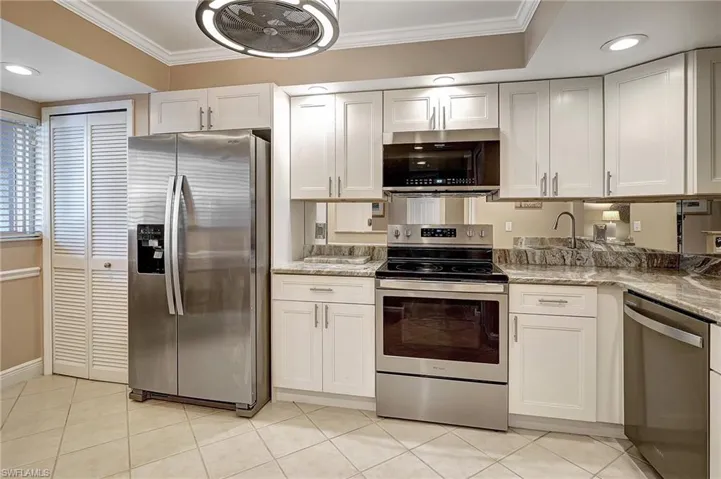 Kitchen with light stone countertops, ornamental molding, stainless steel appliances, light tile patterned floors, and white cabinets