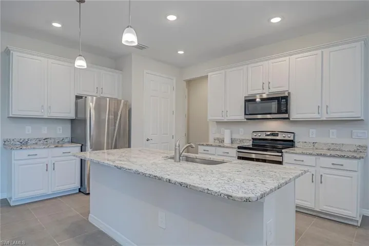Kitchen featuring stainless steel appliances, white cabinets, a kitchen island with sink, and light stone counters