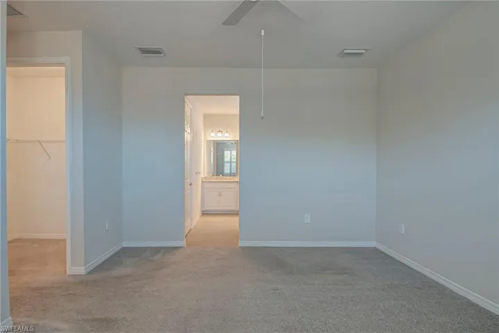 Primary bedroom with a spacious closet, light colored carpet, and ceiling fan