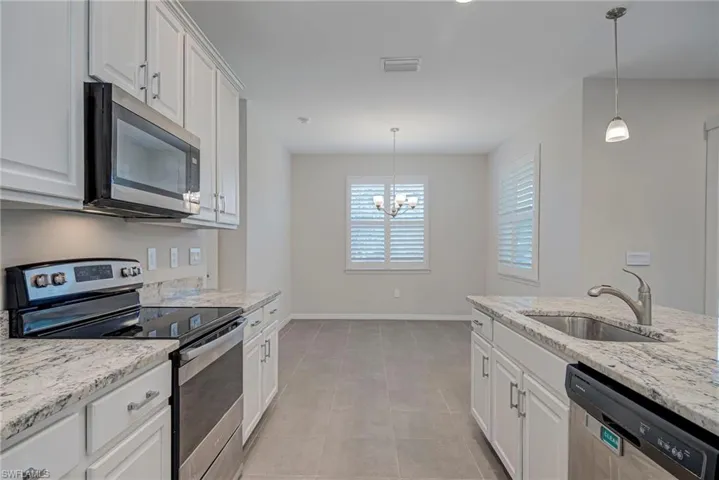 Kitchen featuring stainless steel appliances, white cabinets, light stone countertops, and suspended lighting