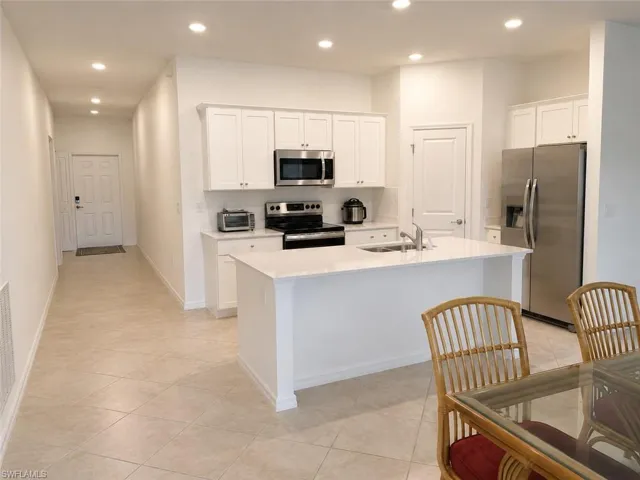 Kitchen featuring white shaker cabinetry, stainless steel appliances, a center island with sink, and tile flooring
