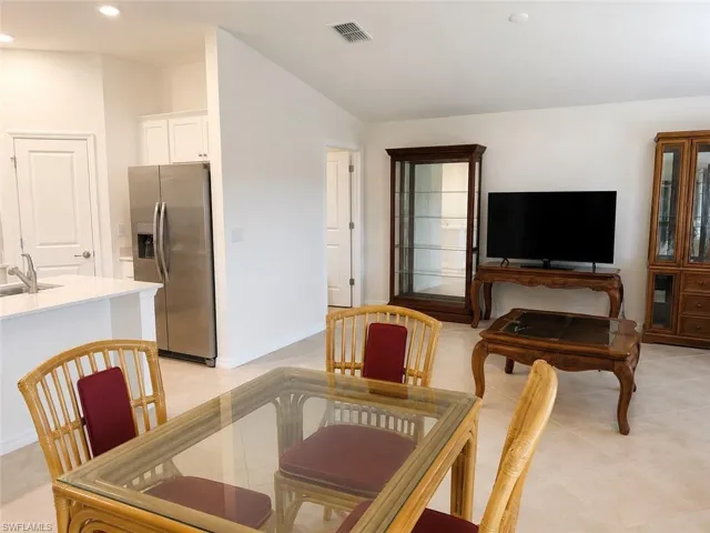 Open-concept layout with recessed lighting, tile flooring, white shaker cabinetry, stainless steel refrigerator, and a kitchen island with a sink
