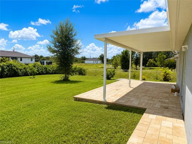Expansive backyard with a manicured lawn, shade tree, and a paver patio featuring a covered overhang
