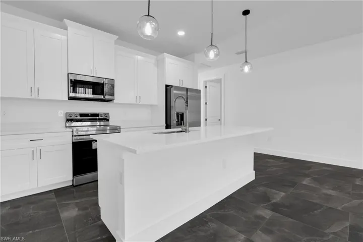 Kitchen with stainless steel appliances, white cabinetry, hanging light fixtures, a kitchen island with sink, and light stone countertops