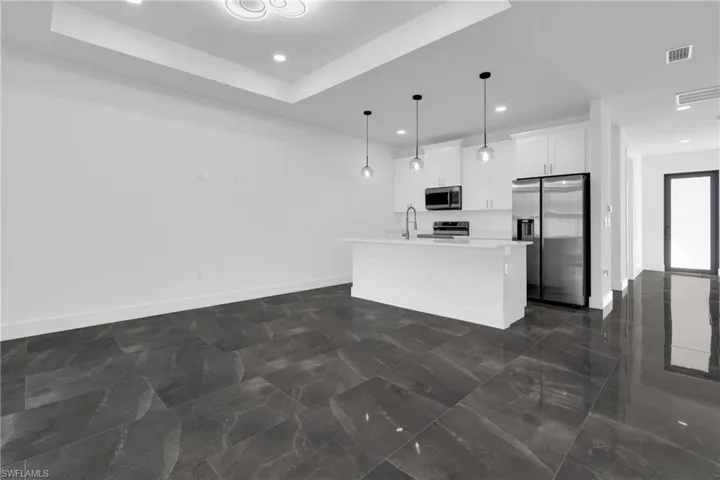 Kitchen with stainless steel appliances, a center island with sink, white cabinets, hanging light fixtures, and open floor plan
