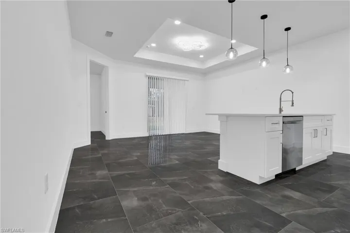 Kitchen with hanging light fixtures, a raised ceiling, an island with sink, white cabinets, and stainless steel dishwasher