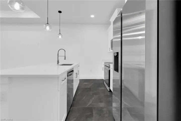 Kitchen with stainless steel appliances, white cabinets, light stone counters, decorative light fixtures, and a kitchen island with sink