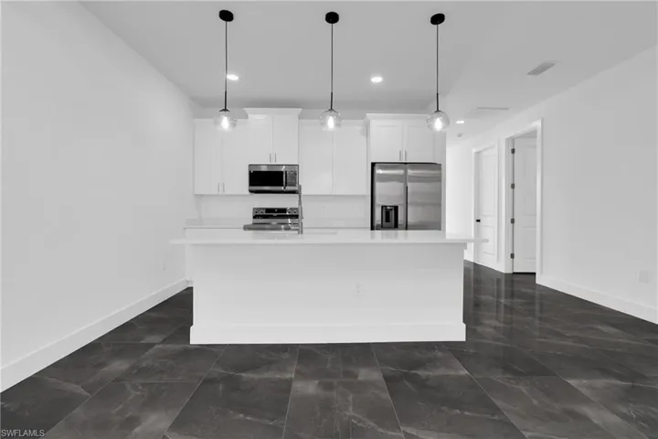 Kitchen with stainless steel appliances, white cabinetry, an island with sink, and pendant lighting