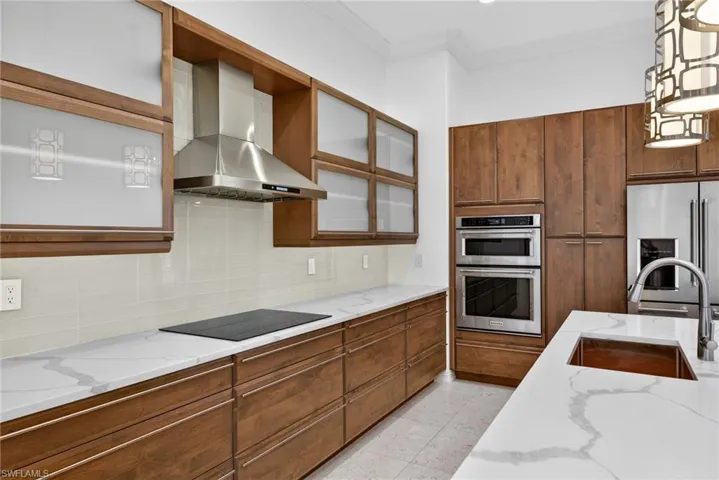 Kitchen featuring brown cabinetry, wall chimney exhaust hood, light stone countertops, and ornamental molding