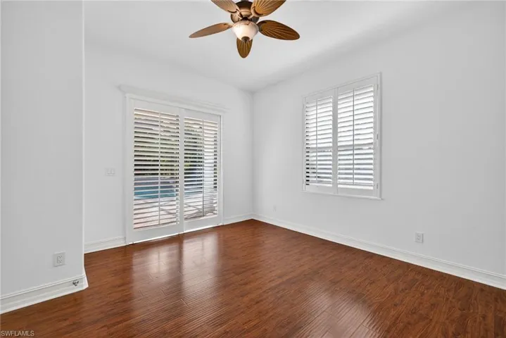 Empty room with dark wood-type flooring, plenty of natural light, and a ceiling fan