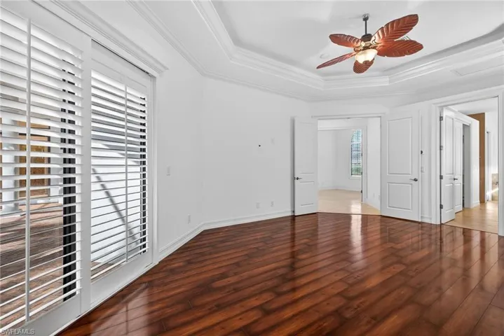 Unfurnished bedroom featuring crown molding, dark wood-type flooring, ceiling fan, and a tray ceiling