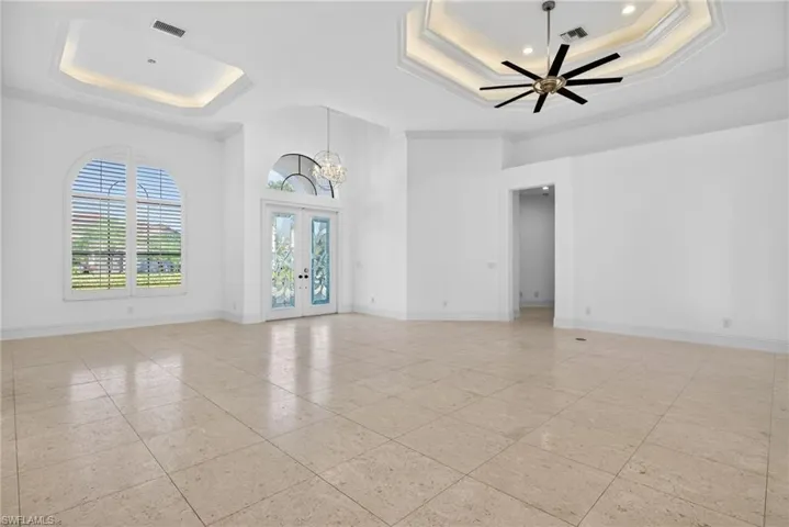 Empty room with french doors, crown molding, a tray ceiling, a chandelier, and ceiling fan