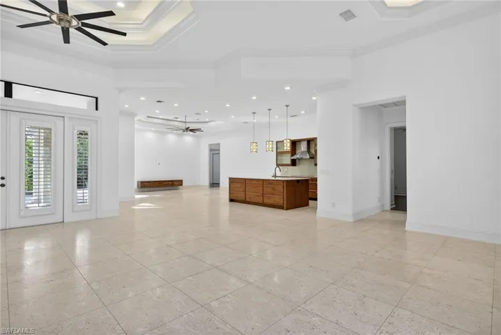 Unfurnished living room featuring a ceiling fan, a raised ceiling, recessed lighting, and ornamental molding