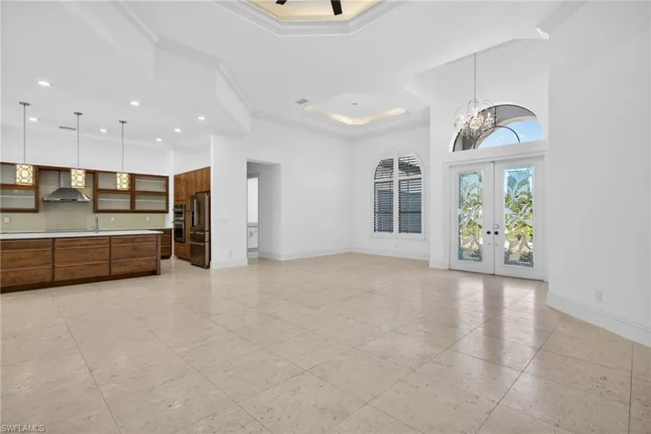 Unfurnished living room featuring french doors, crown molding, a tray ceiling, and a chandelier