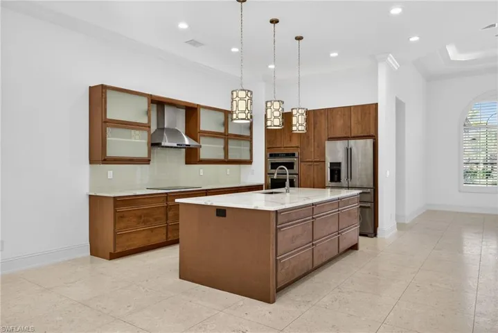 Kitchen featuring hanging light fixtures, decorative backsplash, stainless steel appliances, wall chimney range hood, and light stone countertops