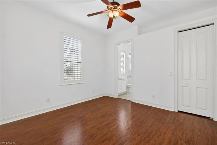 Unfurnished bedroom featuring dark wood finished floors, a ceiling fan, a closet, and ensuite bath