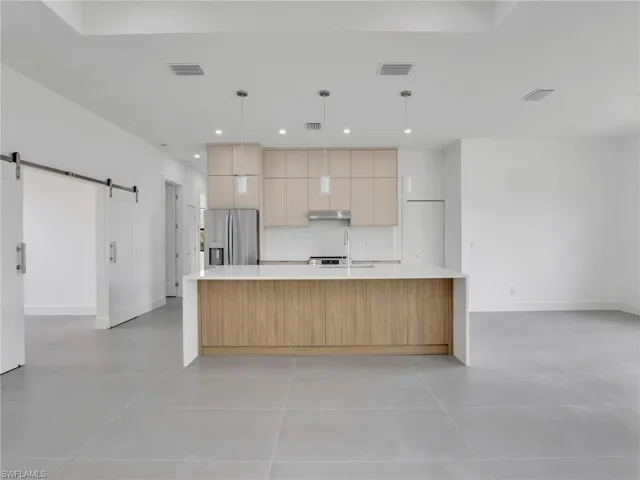 Kitchen with a barn door, a large island with sink, pendant lighting, light stone counters, and stainless steel refrigerator with ice dispenser