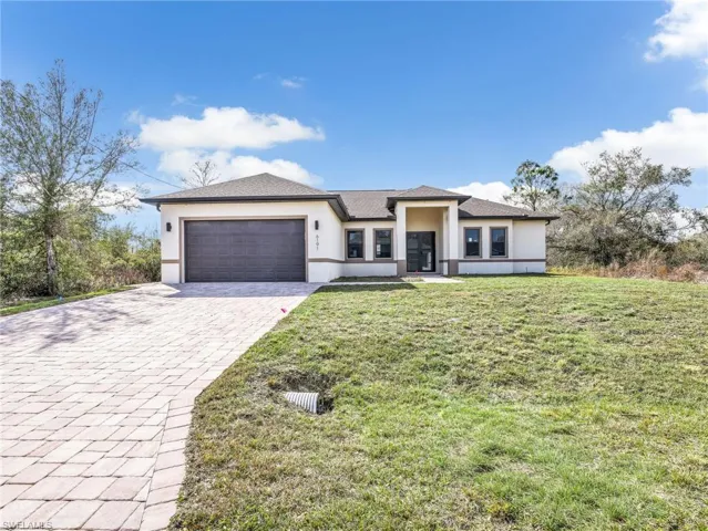 Prairie-style home featuring stucco siding, decorative driveway, an attached garage, and a front yard