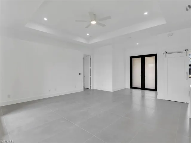 Unfurnished room featuring a barn door, a ceiling fan, french doors, recessed lighting, and a raised ceiling