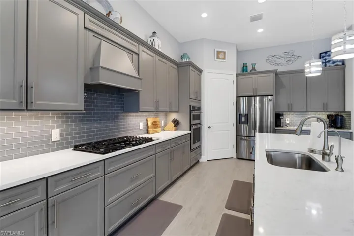 Kitchen with custom exhaust hood, backsplash, appliances with stainless steel finishes, pendant lighting, and sink