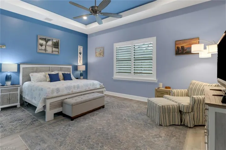 Bedroom with a raised ceiling, wood-type flooring, and ceiling fan