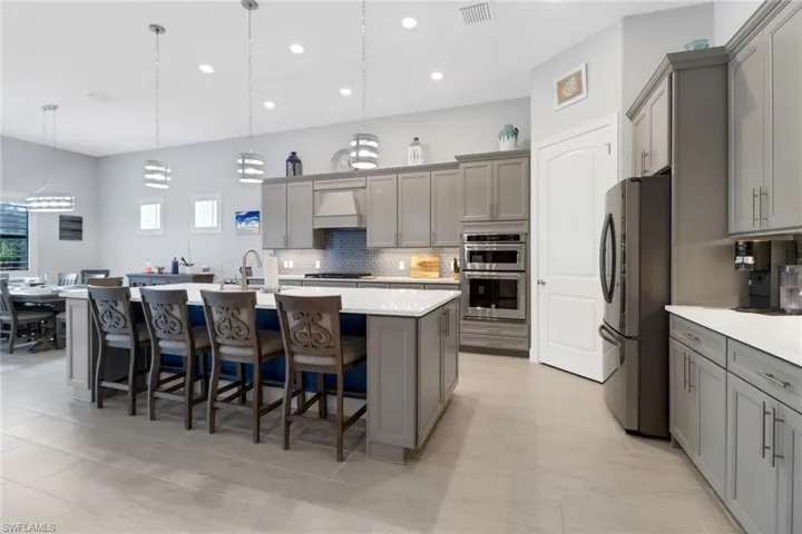 Kitchen featuring gray cabinets, a kitchen island with sink, appliances with stainless steel finishes, and decorative light fixtures