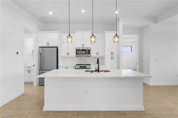 Kitchen featuring stainless steel appliances, white cabinets, a kitchen island with sink, and sink