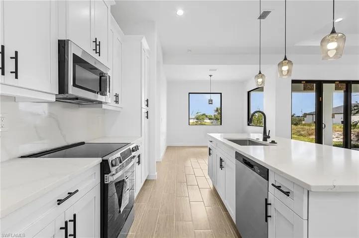 Kitchen featuring hanging light fixtures, an island with sink, white cabinets, stainless steel appliances, and sink