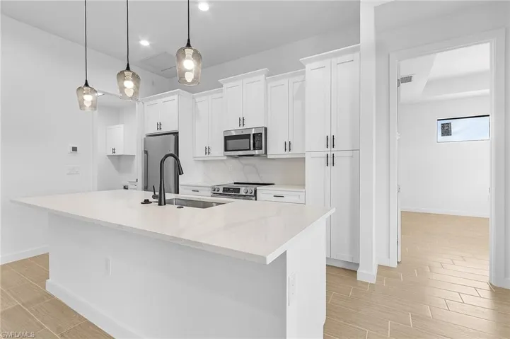 Kitchen with a kitchen island with sink, stainless steel appliances, white cabinets, and decorative light fixtures