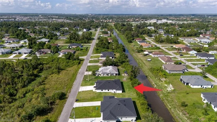 Canal-front property featuring a developed residential street, surrounding green spaces, and a distant urban landscape