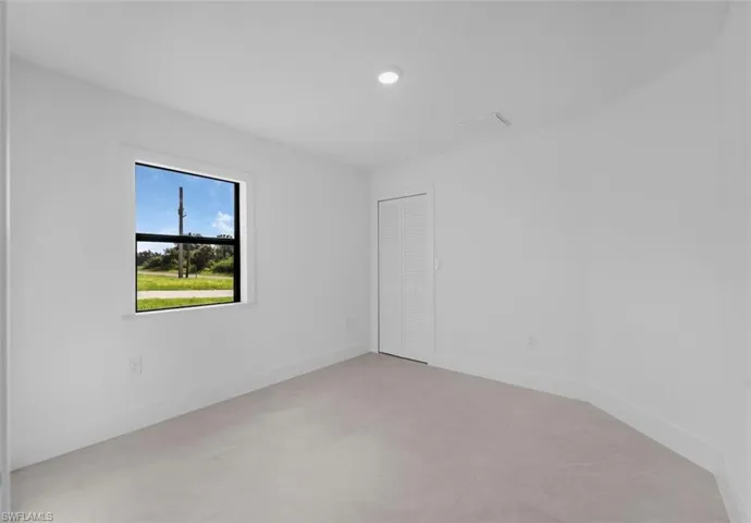 Room featuring light-toned flooring, white walls, and a single window with a black frame