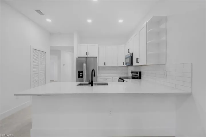 Modern kitchen featuring a large white countertop island, stainless steel appliances, white cabinetry with black hardware, a subway tile backsplash, and recessed lighting