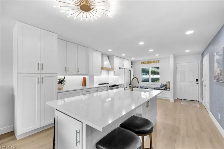 Kitchen featuring wall chimney range hood, sink, an island with sink, and white cabinets
