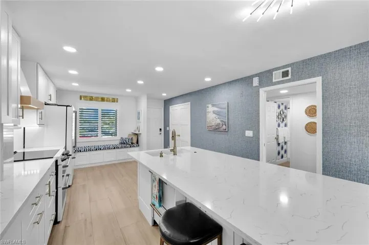 Kitchen with range with electric stovetop, light stone countertops, sink, and white cabinets