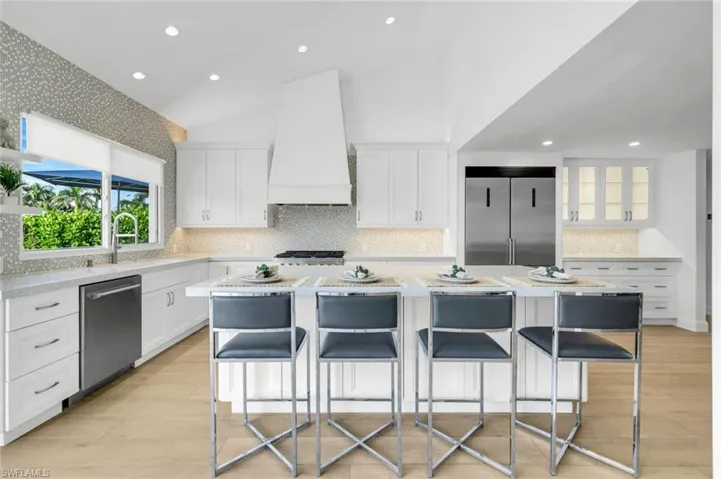 Kitchen featuring tasteful backsplash, white cabinets, recessed lighting, light stone counters, and a center island