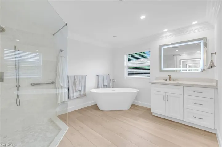 Full bathroom featuring vanity, walk in shower, light wood finished floors, a freestanding bath, and crown molding