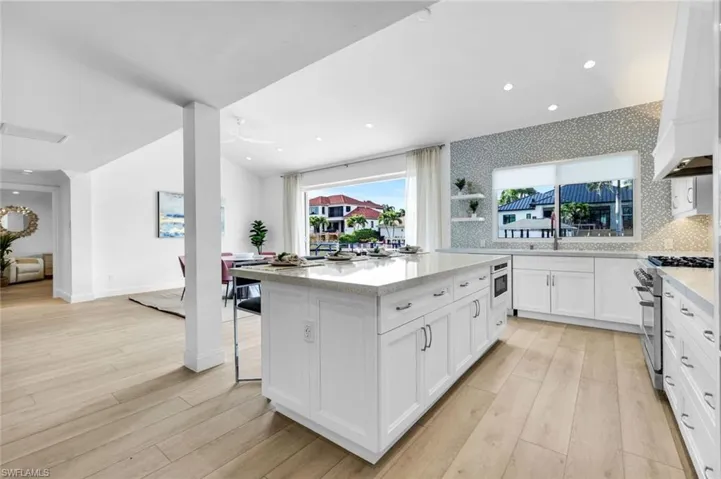 Kitchen with white cabinetry, light stone countertops, a kitchen island, a kitchen breakfast bar, and light wood finished floors
