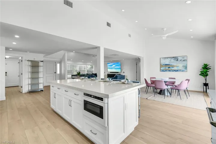 Kitchen with recessed lighting, white cabinets, light wood-style floors, a kitchen island, and light stone counters