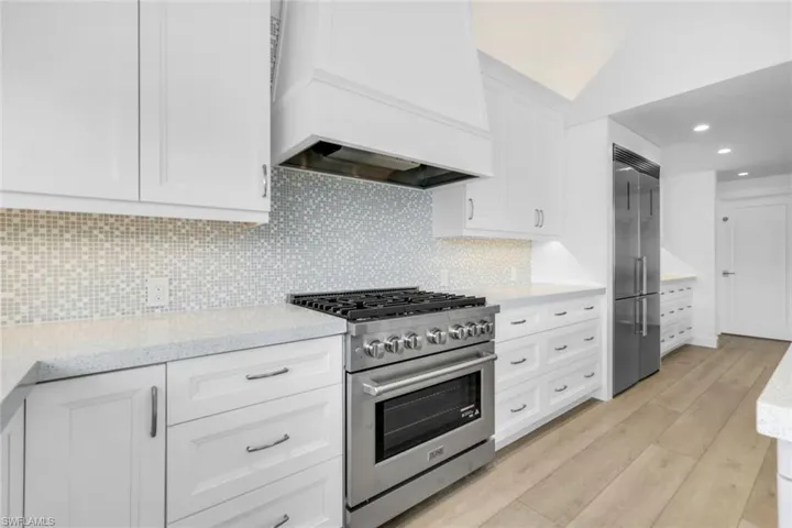 Kitchen with high end appliances, white cabinetry, custom range hood, recessed lighting, and light stone counters