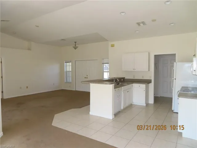 Kitchen with open floor plan, a peninsula, white cabinets, light carpet, and light tile patterned floors