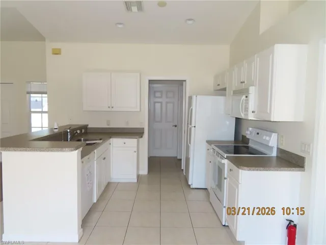 Kitchen featuring a peninsula, white appliances, dark countertops, white cabinetry, and light tile patterned flooring