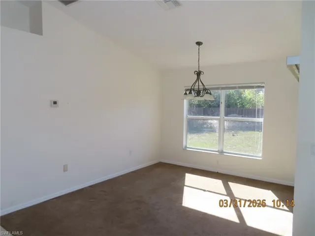 Spare room featuring dark colored carpet and a chandelier